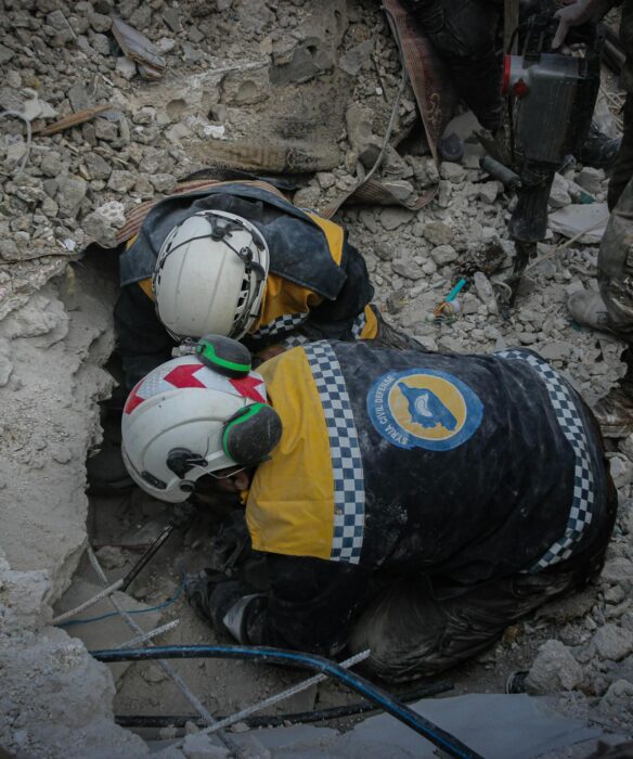 Rescue workers from civil defense searching rubble for survivors in Idlib, Syria, post-disaster.